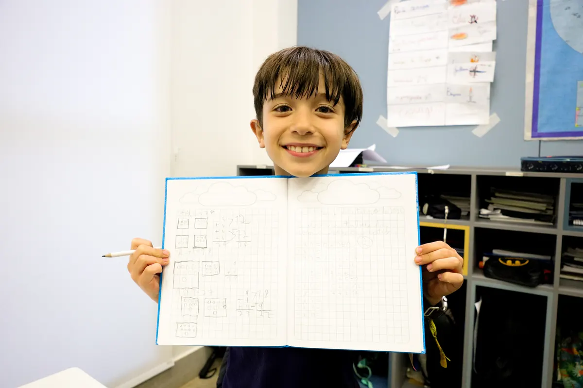 Aluno do 1º ano sorrindo e mostrando o caderno