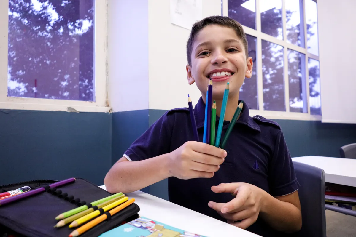 Aluno sorrindo segurando lápis de cor na sala de aula