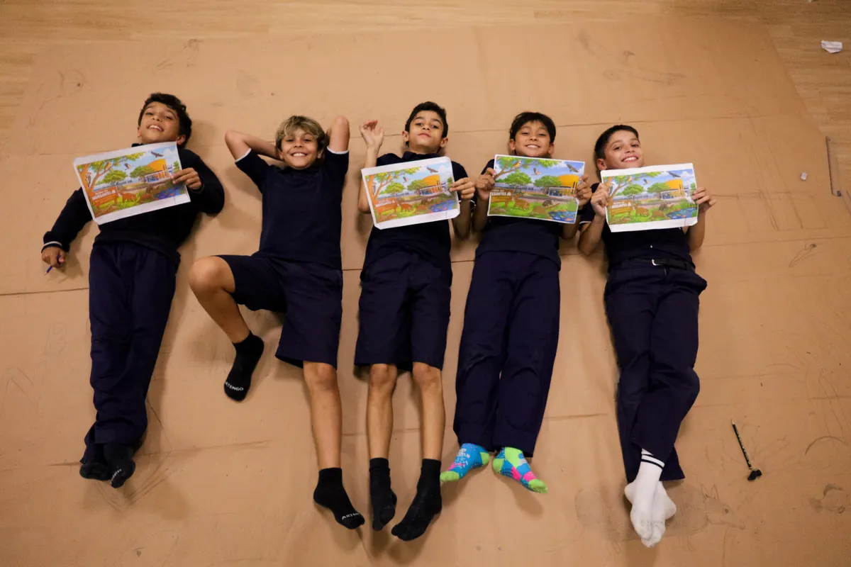 Cinco alunos deitados no chão mostrando seus desenhos