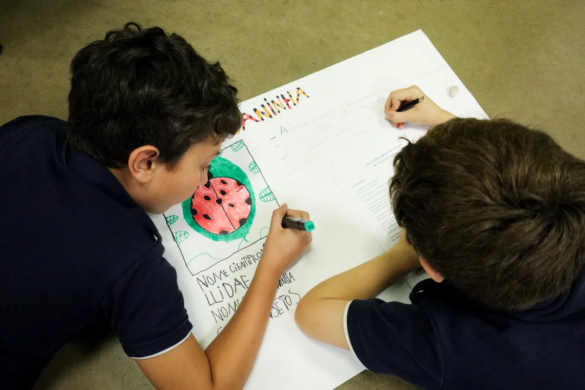 Dois alunos desenhando juntos em um cartaz
