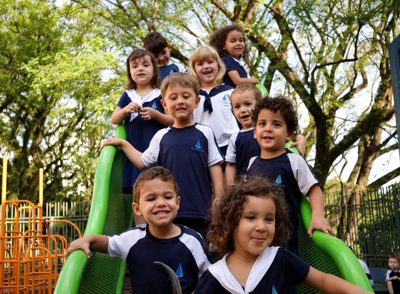 Grupo de crianças sorrindo descendo o tobogã do parque sob as árvores